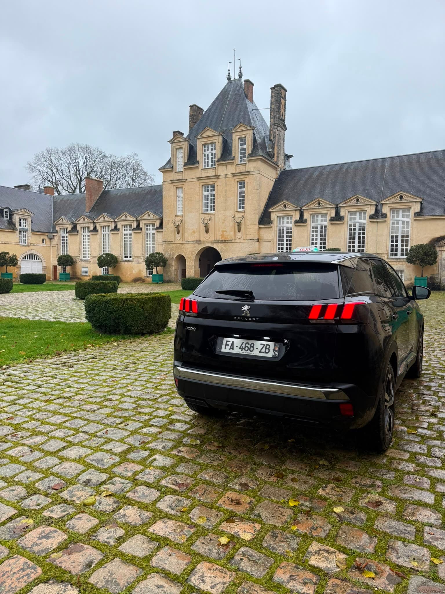 Le taxi TSM, Peugeot 3008 noir, feux allumés dans la cour pavée d'un château